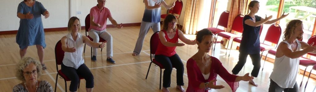 A group of people in a Tai Chi Movements for Wellbeing class, some seated and some standing.