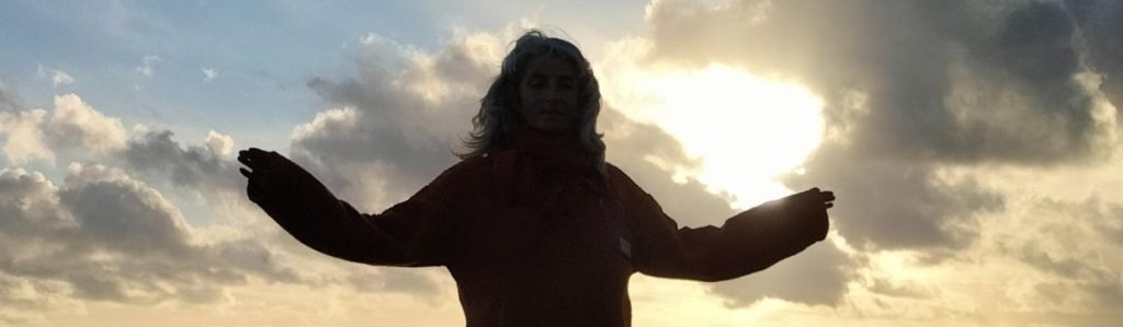 Woman doing Tai Chi Movements for Wellbeing on beach with cloudy sky in background.
